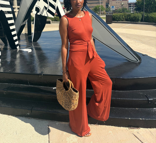 Woman in a red jumpsuit holding a straw bag, standing in front of a black sculpture.