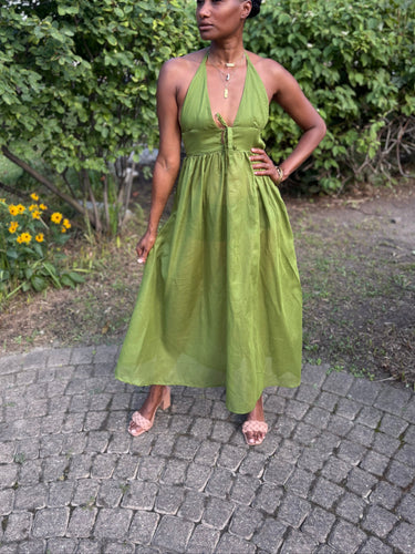 Woman in a green dress standing outdoors on a paved path with greenery in the background